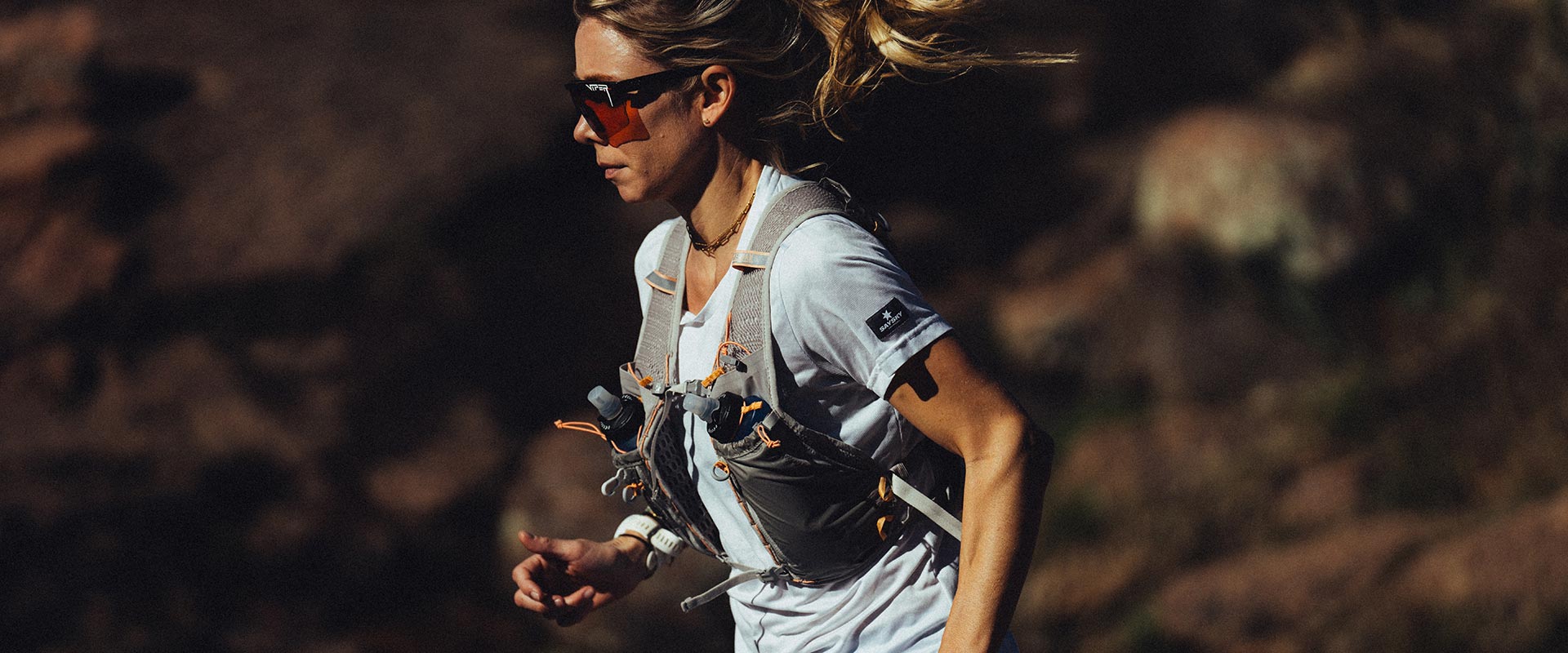 Person running with a hydration run vest and sunglasses in a natural setting