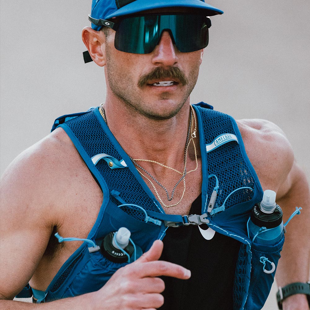 Man wearing a blue running vest with water bottles during a run